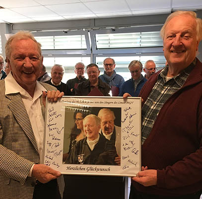 Von links: Jubilar, Peter Labonte sowie der 1. Vorsitzende des MGV Linz, Norbert Klein. Im Hintergrund einige Snger vom Mnnergesangverein Linz. Foto: Roland Thees