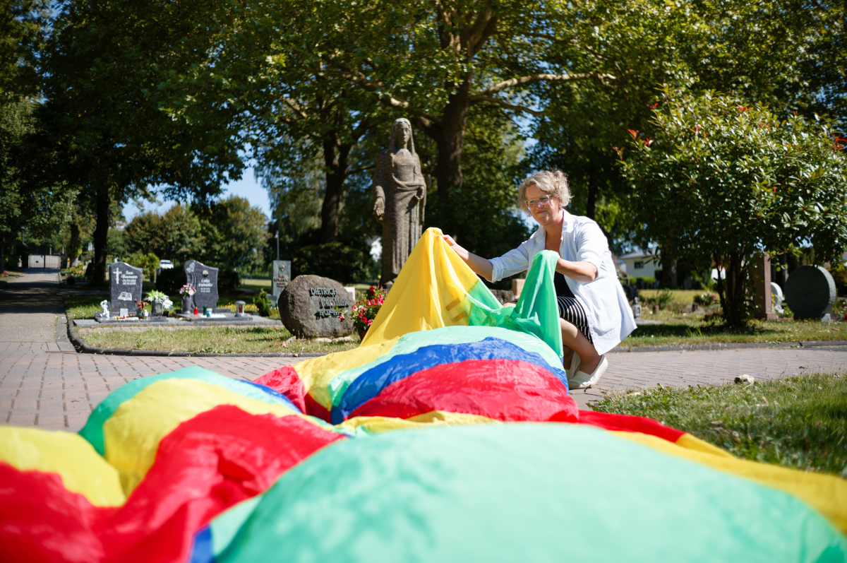 Mit Kindern auf dem Friedhof ber das Sterben und den Himmel reden: Pfarrerin Monika Christ (Foto) findet, dass das eine bereichernde Erfahrung sein kann. Das bunte Tuch gehrt zu den Treffen der "Kinderkirche" mit dazu - auch am 7. September, wenn sich alle auf dem Westfriedhof in Hhr-Grenzhausen treffen. 
(Foto: Dekanat Westerwald)