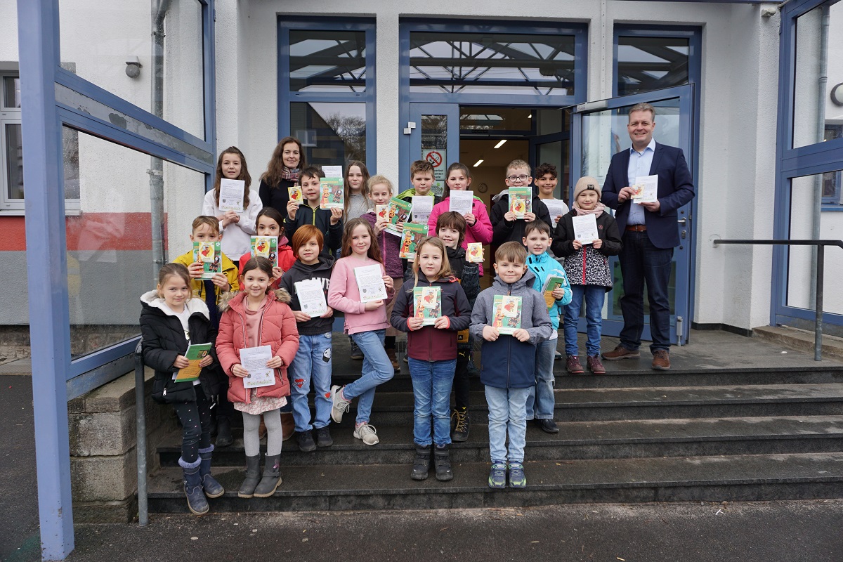 Brgermeister Gerrit Mller (oben rechts) berreicht die Blumensamen und Kinderbcher an die Konrektorin Tamara Eickmeier (hinten links) und einer Vertretung aus Klassensprechern der Grundschule Steinsbergschule Rennerod. (Foto: Bianca Weber)