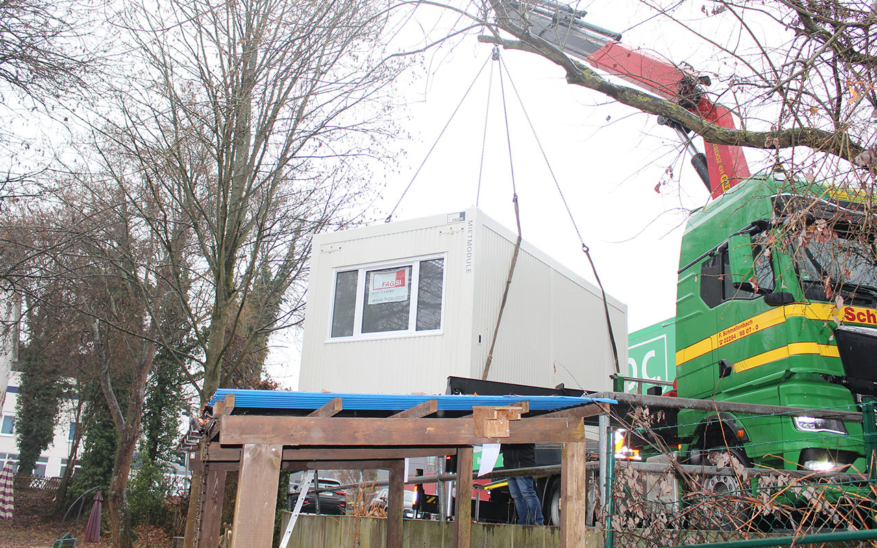 Per Ladekran und an vier Ketten befestigt schwebt der Raumcontainer ber den Zaun auf dem Innenhof des Caf Patchwork ein. (Foto: Diakonie)